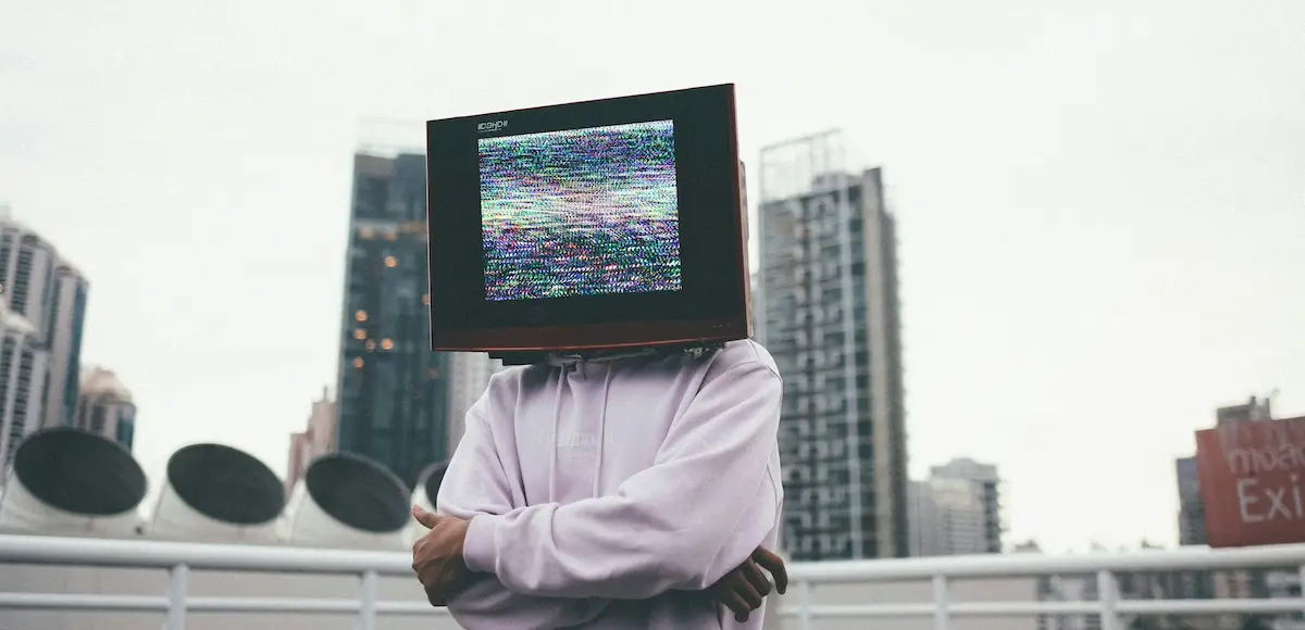 Mann mit Pulli und einem Monitor als Kopf vor einer urbanen Kulisse